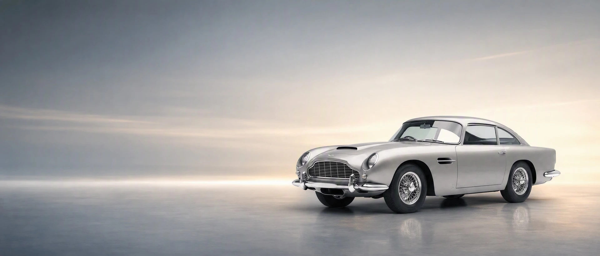 A silver Aston Martin DB5, front three-quarter view on a silver-champagne field