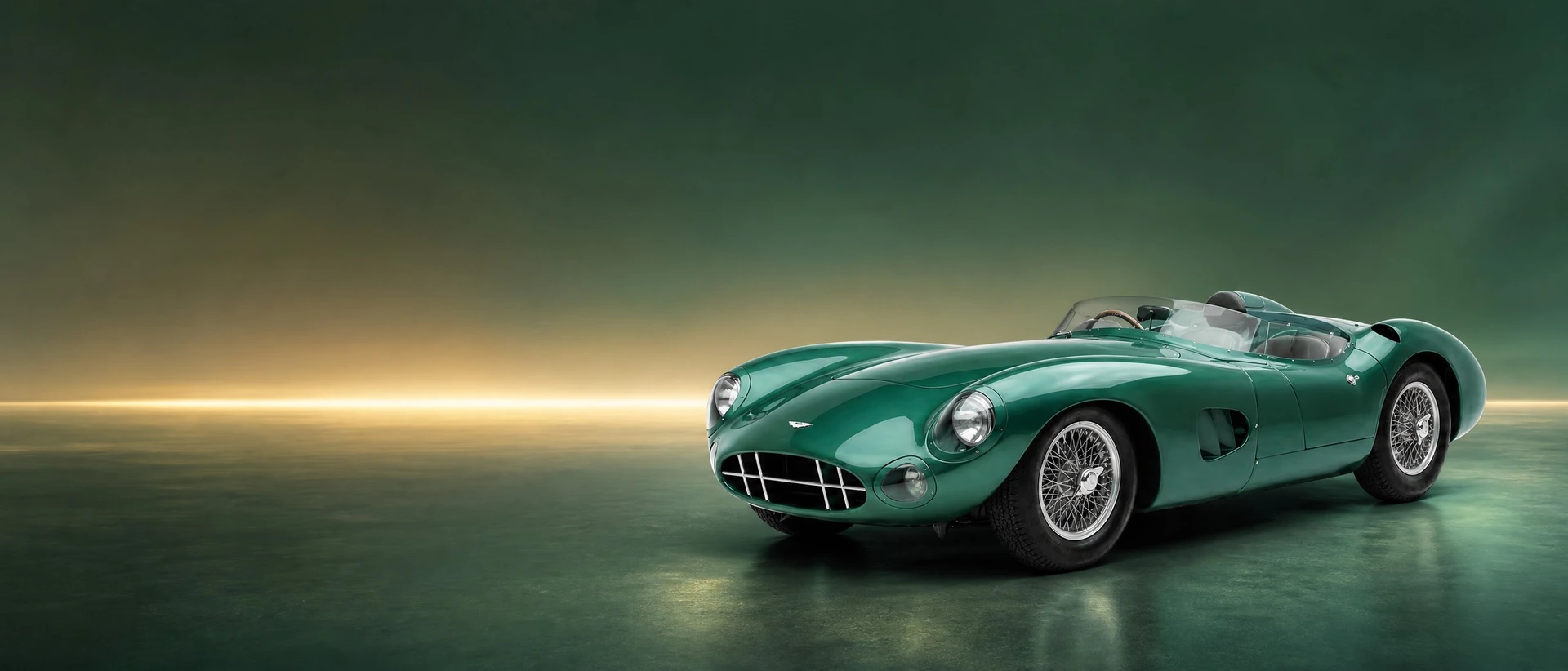 An Aston Martin DBR1 sports-racer in green, front three-quarter view on a green field with a gold dawn glow