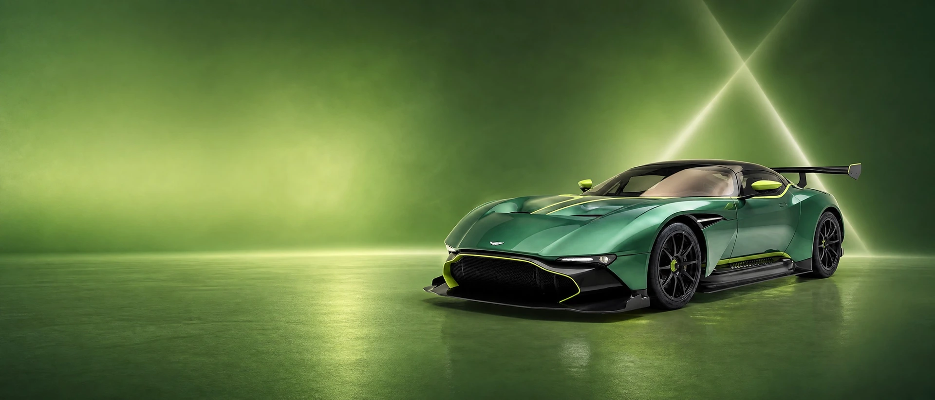 A green Aston Martin Vulcan, front three-quarter view on a moss-green field with crossing shafts of light