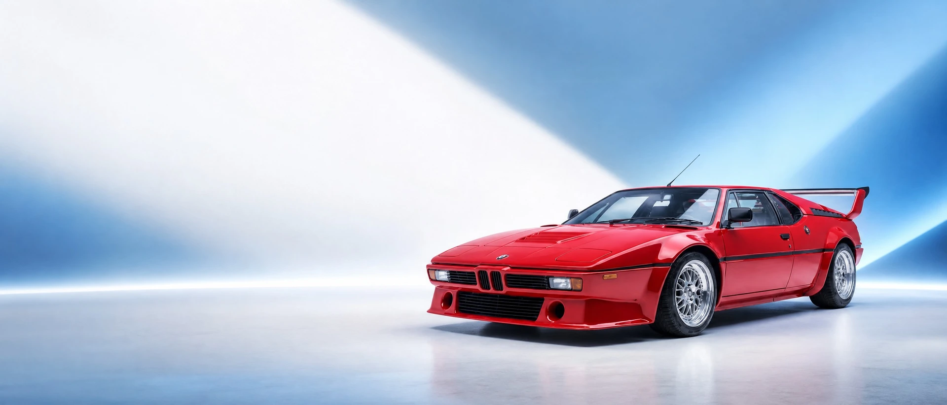 A red BMW M1, front three-quarter view on a white field with motorsport light wedges