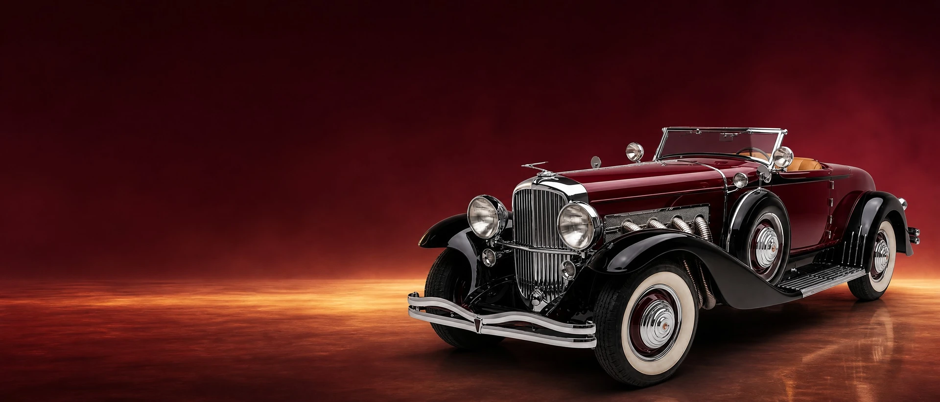 A burgundy and black Duesenberg Model J roadster, front three-quarter view on a burgundy field with golden light