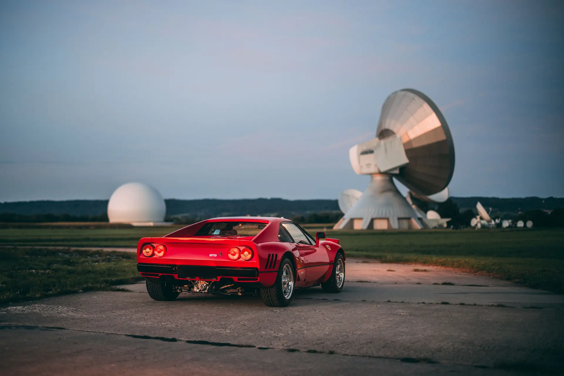 Red Ferrari 288 GTO in rear-three-quarter view beside a radome at dusk