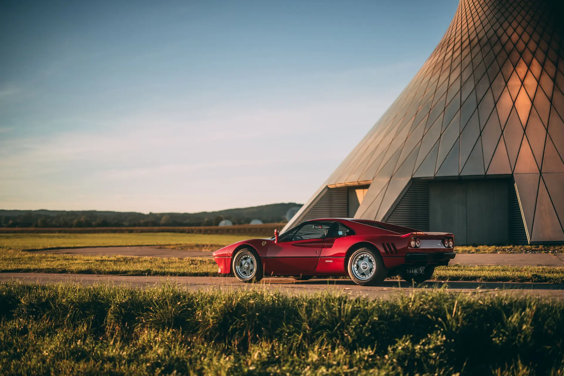 Rosso Corsa Ferrari 288 GTO in rear-three-quarter view beside a pyramid structure