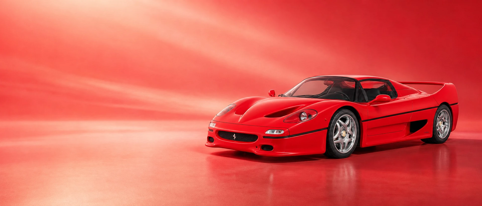 A Rosso Corsa Ferrari F50, front three-quarter view on a warm rosso field in soft sunlight