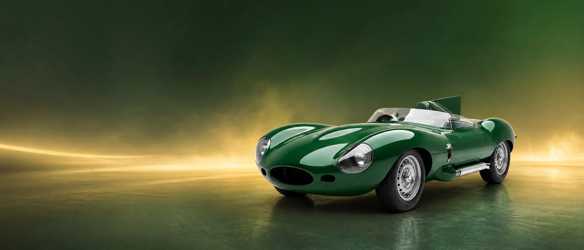 A British Racing Green Jaguar D-Type, front three-quarter view on a green-gold field with glowing mist
