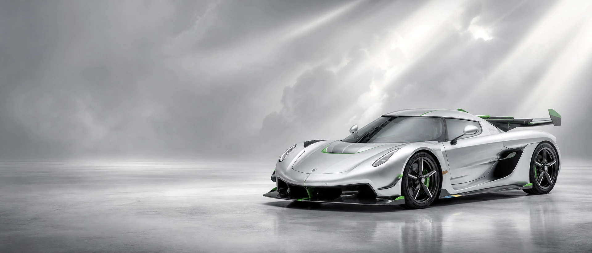A silver Koenigsegg Jesko with green accents, front three-quarter view on a silver field with breaking light beams