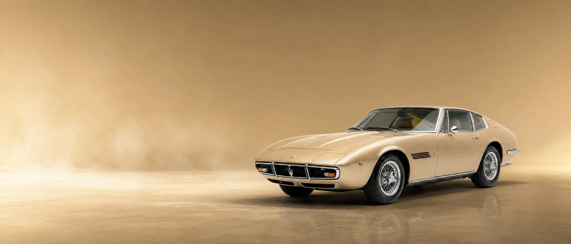 A first-generation Maserati Ghibli, front three-quarter view on an amber field with sand-light haze