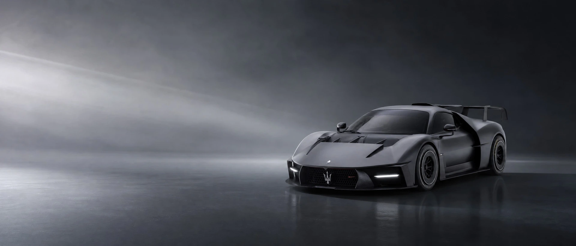 A dark grey Maserati MCXtrema, front three-quarter view on a graphite field with a wide cold beam
