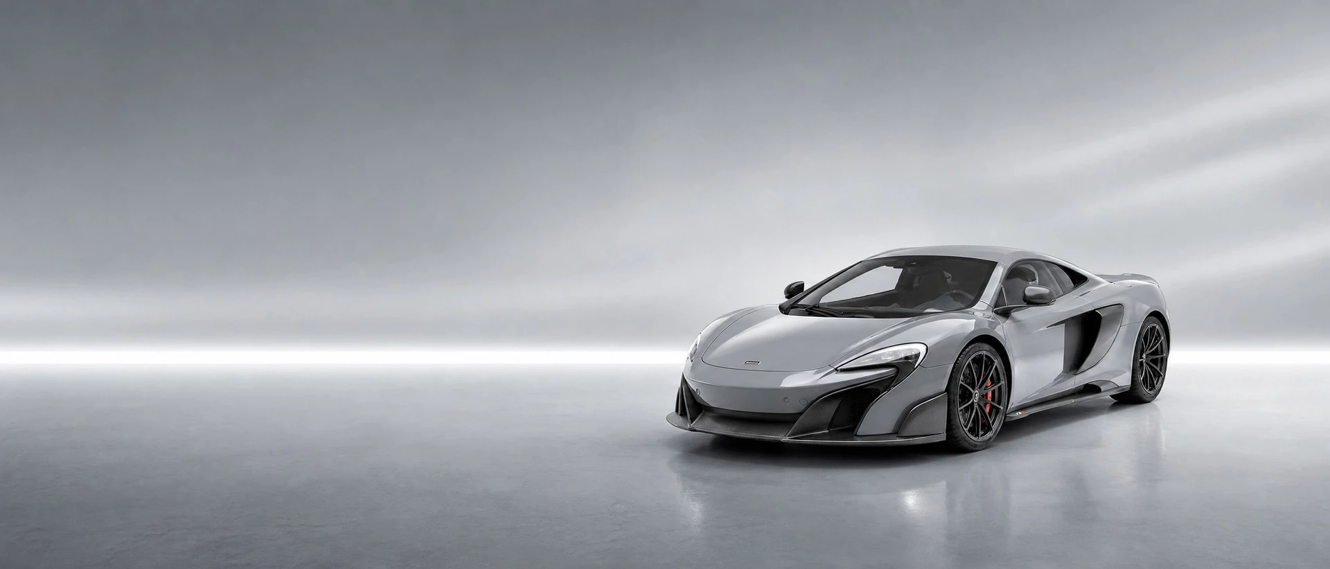 A silver-grey McLaren 675LT, front three-quarter view on a silver field with a sharp bar of light