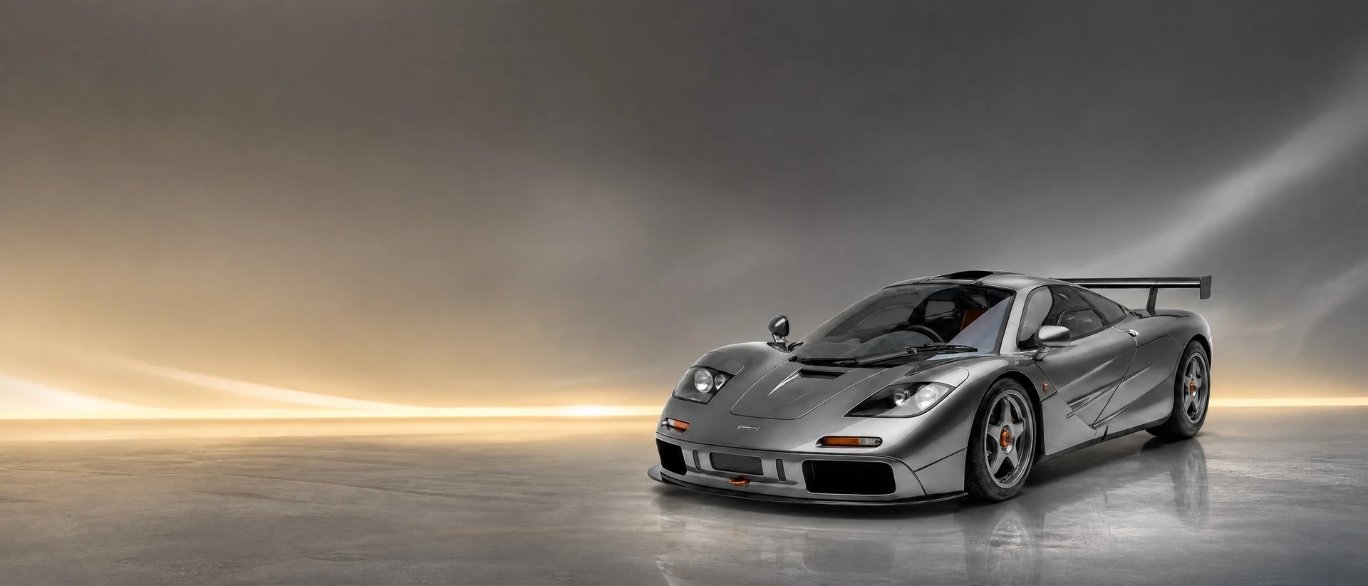 A grey McLaren F1 GTR, front three-quarter view on a pewter field with a warm gold glow