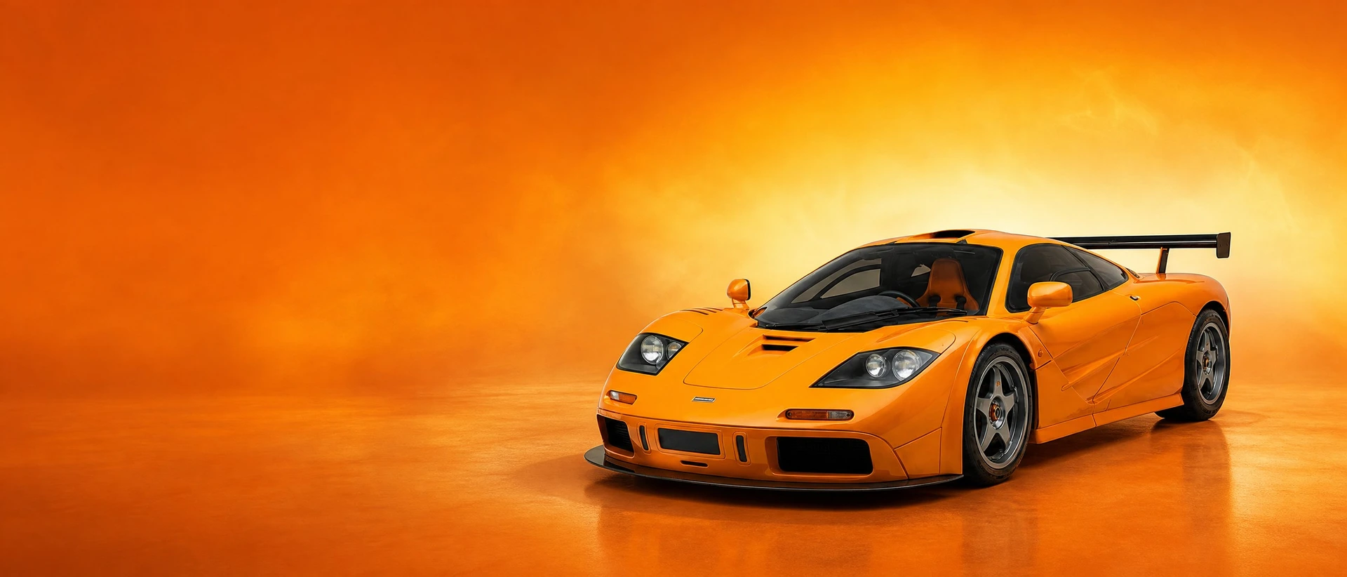 An orange McLaren F1 LM, front three-quarter view on a papaya-orange field with a wide bloom of light