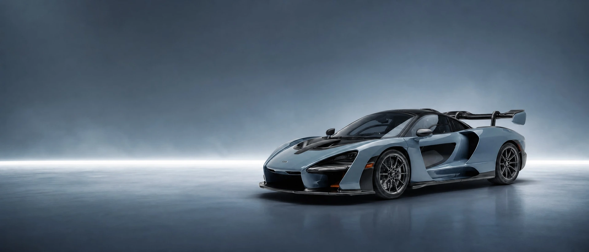 A dark blue-grey McLaren Senna, front three-quarter view on a graphite-blue field with a severe bar of light