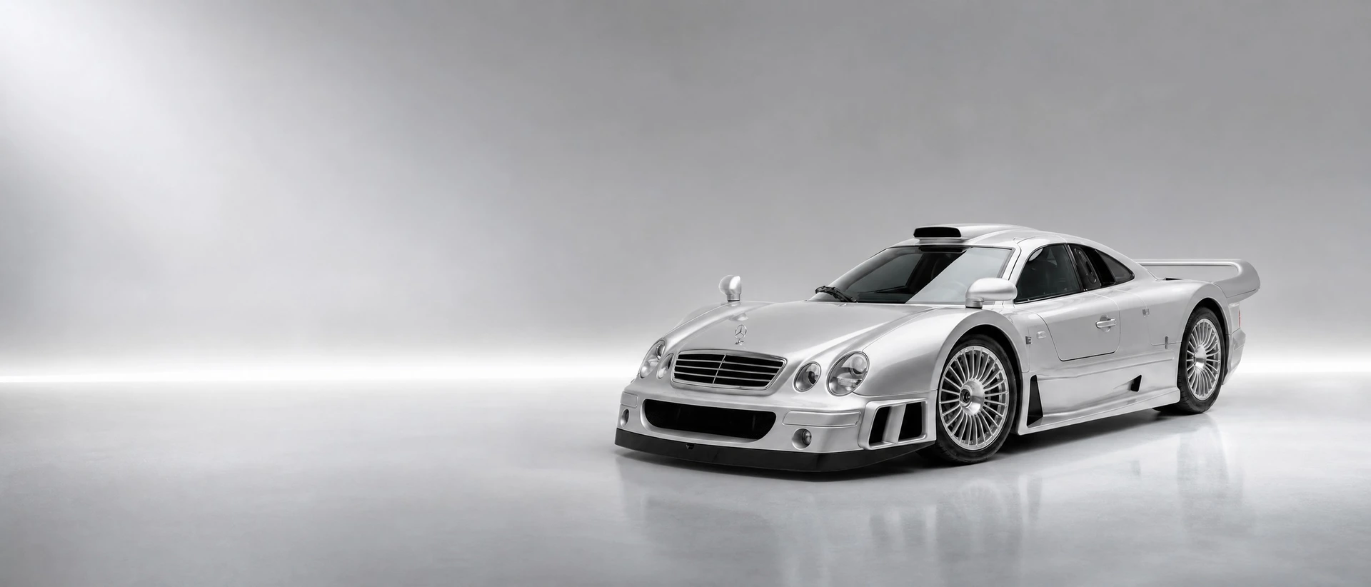 A silver Mercedes-Benz CLK GTR Straßenversion, front three-quarter view on a silver field with a white light bar