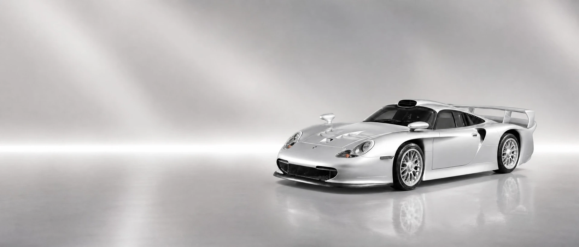 A silver Porsche 911 GT1 Straßenversion, front three-quarter view on a silver field with a wide light bar