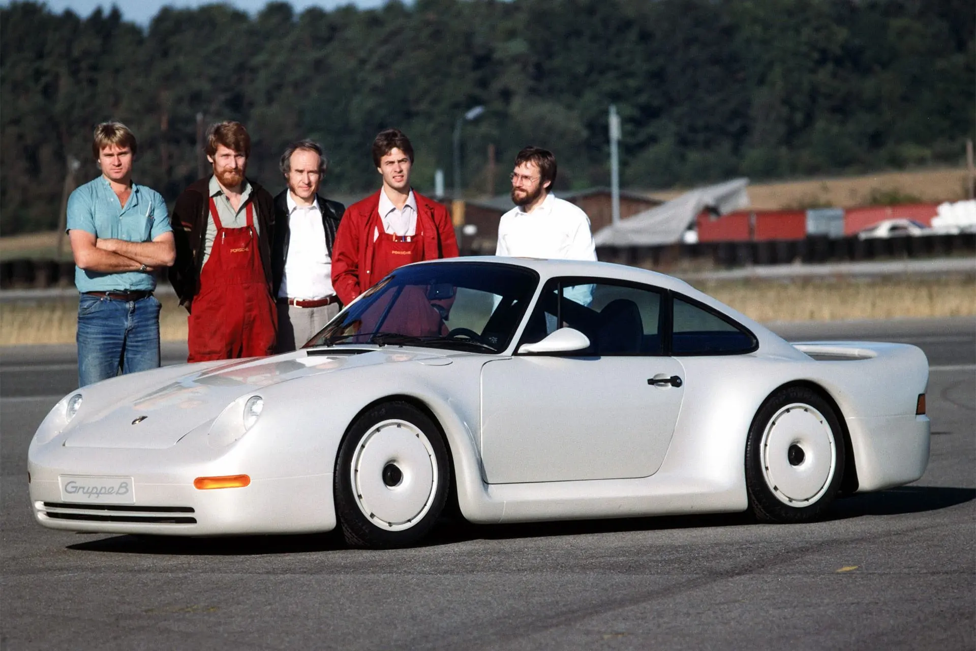 White Porsche Gruppe B study with five team members at an outdoor test facility, front-three-quarter view