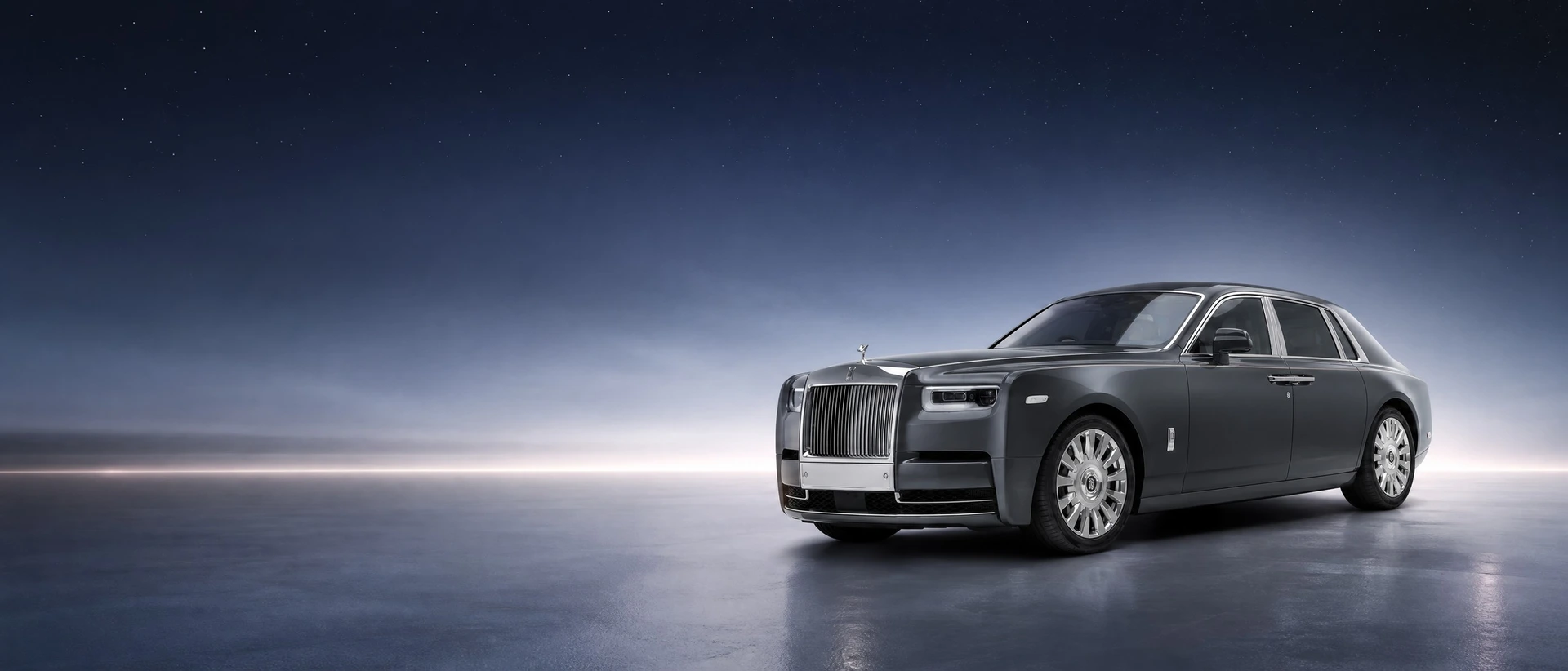 A grey Rolls-Royce Phantom VIII, front three-quarter view under a starlight ceiling at twilight