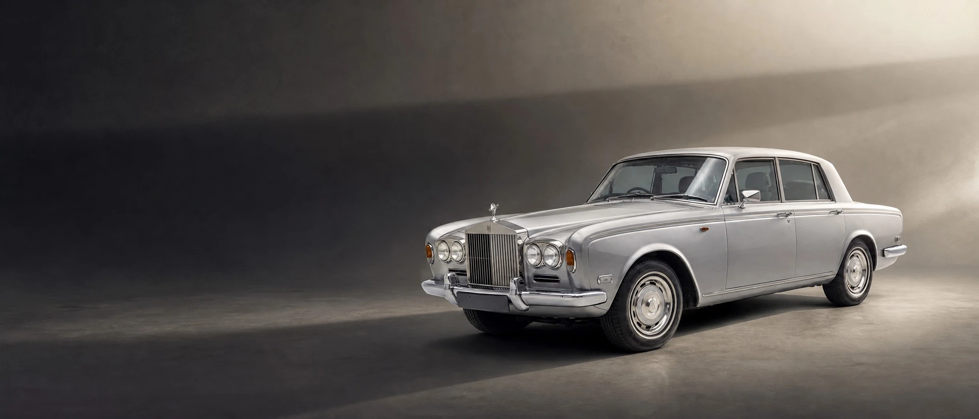 A Rolls-Royce Silver Shadow, front three-quarter view on a graphite field with a long soft shadow