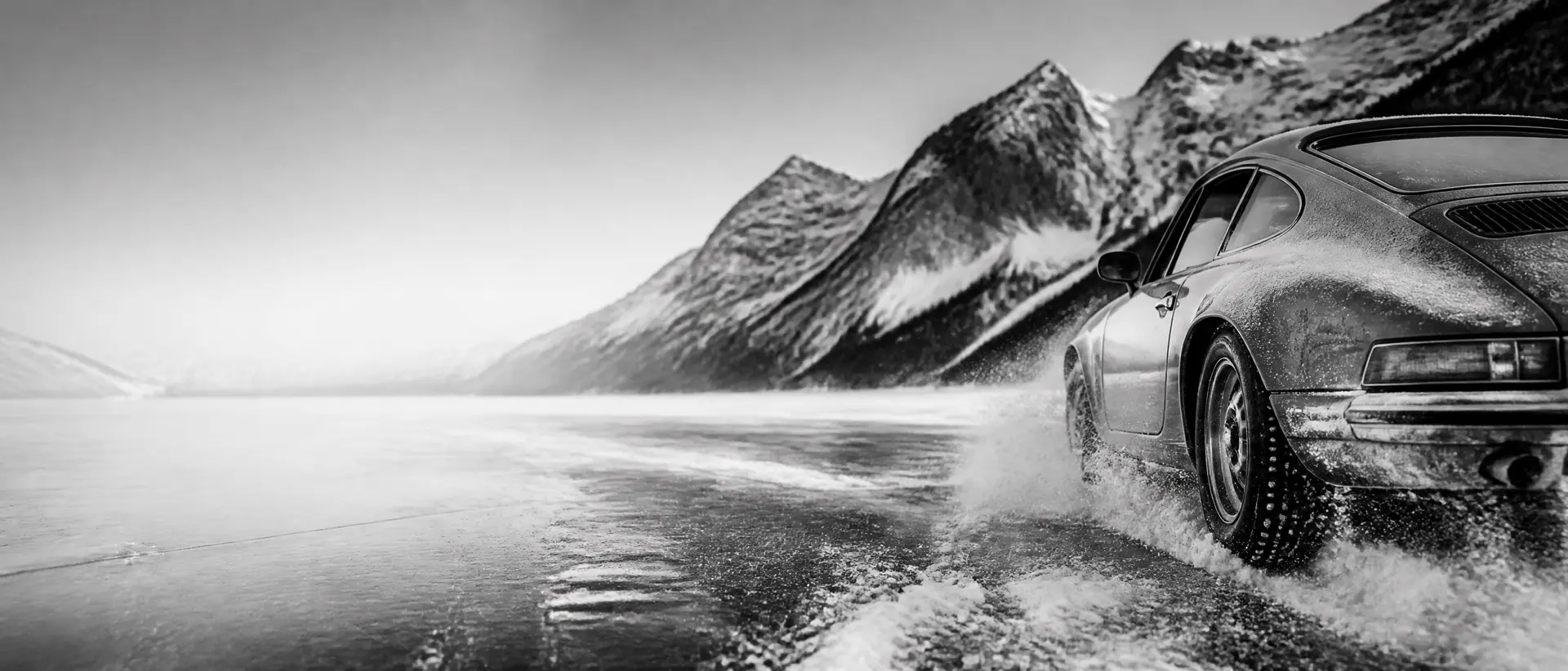 Black-and-white scene of a classic racing car drifting on a frozen lake, snow spray frozen mid-air, Alpine peaks behind, the car’s tail cropped by the frame