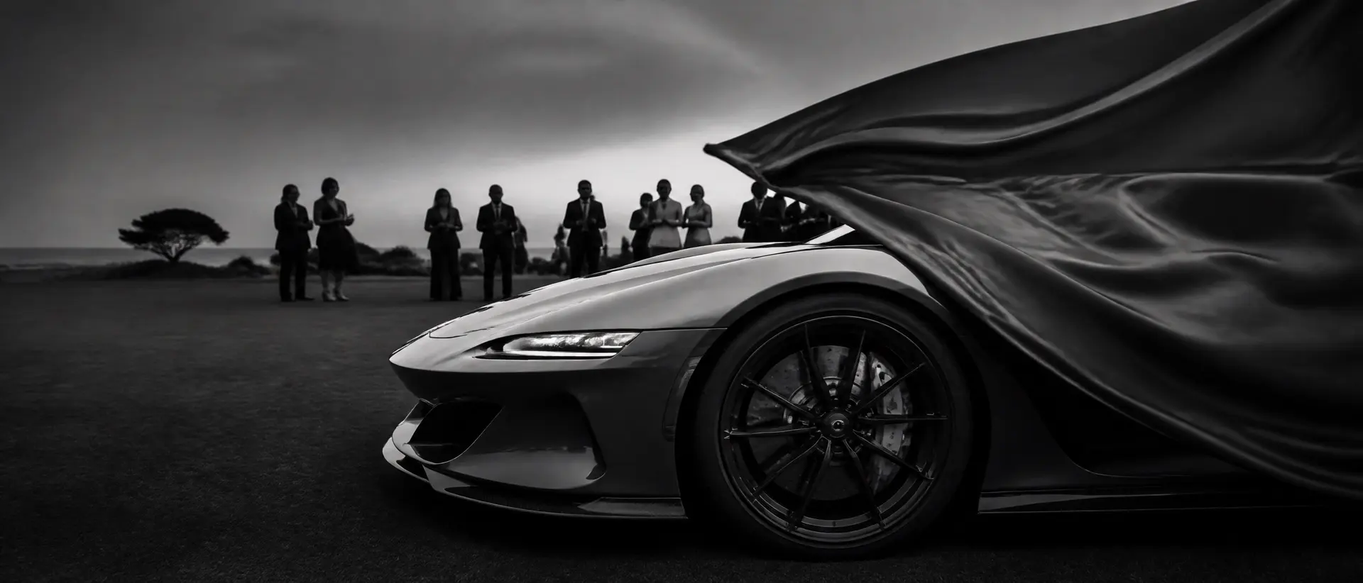 Black-and-white scene of a modern hypercar unveiled on a manicured lawn, silk cover half-lifted, guests in silhouette, the car’s front aero cropped at the left edge