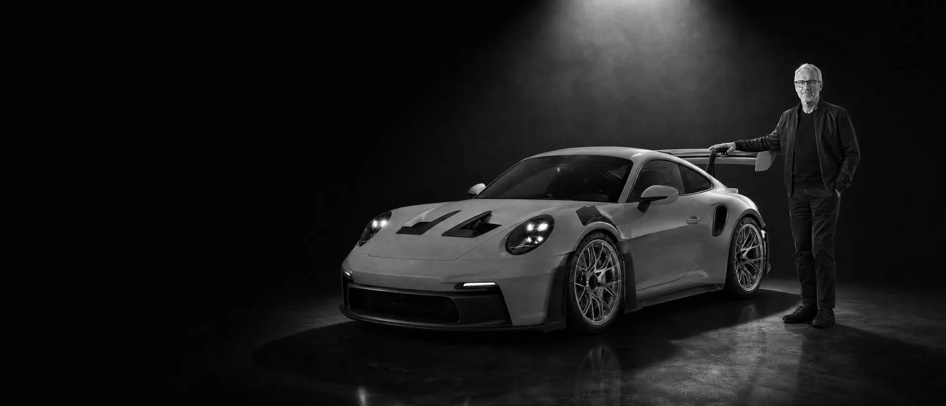 Andreas Preuninger standing beside a Porsche 992 GT3 RS under a single spotlight